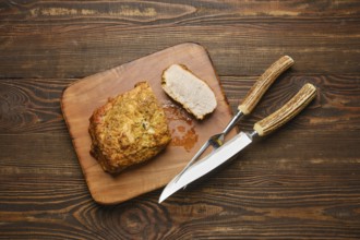 A deliciously roasted piece of pork meat on a wooden cutting board served with carving knife and