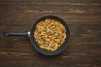 A vibrant mix of fried chanterelles and honey mushrooms in a pan on a wooden table. The colourful