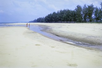 Men walking on sandy beach south of estuary, Rompin, East coast, Pahang, Malaya, Malaysia, south