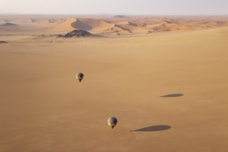 Two hot-air balloons above an arid plain at the edge of the Namib Desert. Aerial view from another