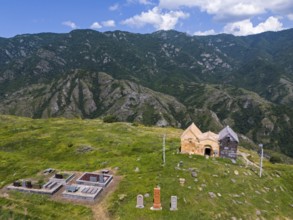 Old church and cemetery on a green mountain under a blue sky with clouds, aerial view, landscape