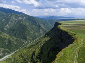 Steep slope with a view of the wide valley and patterned fields under a blue sky, aerial view,