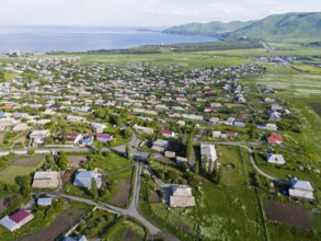 A bird's eye view of a village with scattered houses and green landscape near the coast, aerial