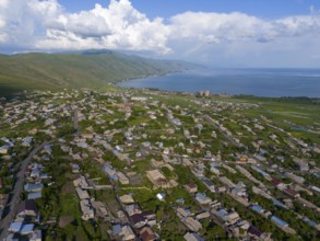 Town with densely packed houses and a view of the sea and mountains under a cloudy sky, aerial