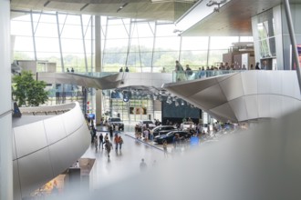 Interior with modern glass structure and people moving between cars, BMW Welt, Munich, Germany