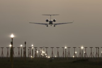 Executive business jet passenger aircraft landing over runway lights at sunset, London Stansted