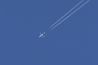 Jet passenger aircraft with a vapour trail or contrail flying in a blue sky, England, United