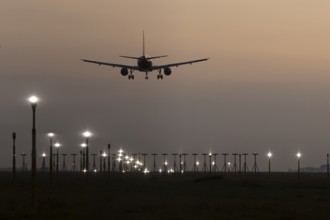 Jet passenger aircraft landing over runway lights at sunset, London Stansted airport, Essex,