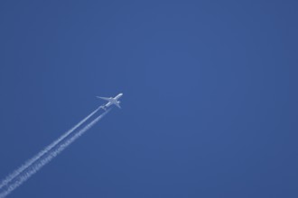 Jet passenger aircraft with a vapour trail or contrail flying in a blue sky, England, United