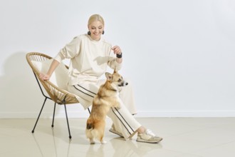 A joyful woman in a light outfit interacts with her playful corgi in a stylish indoor space. The