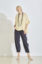A woman stands confidently wearing a stylish yellow blouse and dark pants, accessorized with a