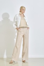 A woman stands confidently wearing a light-colored outfit that includes wide-leg trousers and a
