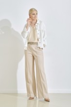 A woman dressed in a cream top and stylish beige trousers strikes a confident pose in a minimalist
