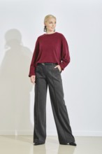 A fashion model stands confidently in a minimalist studio, wearing a maroon sweater and