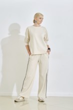 Model poses confidently in a neutral-toned outfit, featuring a sweatshirt and wide-leg pants. Soft