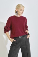 A model stands confidently in a cozy oversized red sweater and tailored dark gray trousers. Her