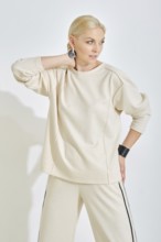 A woman showcases a light-toned casual outfit featuring a relaxed sweatshirt and stylish pants. She