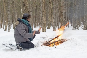 A woman warms herself by a campfire in winter, Gaspesie national park, Province of Quebec, Canada,