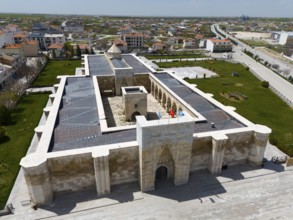 Historic stone caravanserai with courtyard and Tor tor, surrounded by modern urban landscape,
