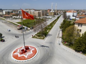 Roundabout with large red flag in urban environment, surrounded by streets and parks, aerial view,