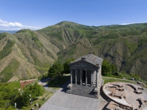 An ancient temple stands against a green mountain backdrop under a blue sky, aerial view, Temple of