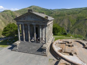 Ancient temple complex with columns and ruins against a green mountain background, aerial view,