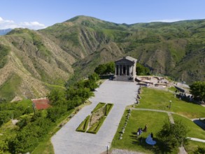 Ancient temple in front of a green mountain backdrop, under a blue sky in a sunny landscape, aerial
