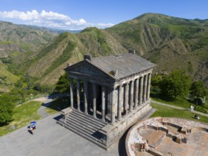 Ancient temple with columns in a green mountain landscape under a blue sky with clouds, aerial