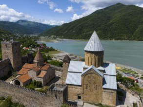 Medieval fortress and church with mountains and river in the background, under blue sky with