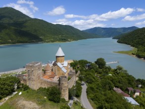 Medieval castle on the river surrounded by green mountains under a cloudy sky, aerial view, Ananuri