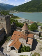 Red tiled roof of a medieval fortress church with castle walls and green lake panorama, aerial