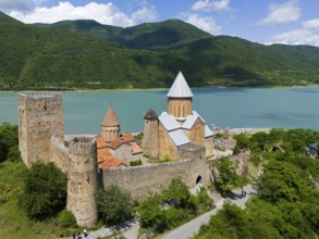 Medieval castle on the lake in front of forested mountains with peaceful atmosphere under blue sky,