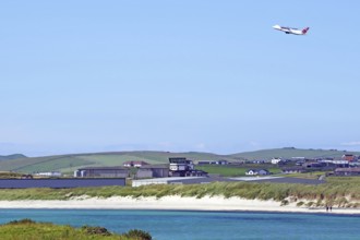 Aeroplane taking off over coast with hangars and green land, Sumburgh Head, Shetland Islands,