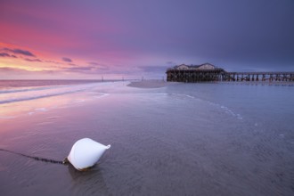 Pile dwellings in St. Peter-Ording in front of the surf in the bright red evening light by the sea