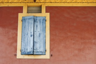 Red house façade with a window and closed blue shutters, Vaison la Romaine, Provence, France
