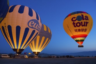 Glowing hot air balloons against a deep blue morning sky create a peaceful atmosphere on a plateau,