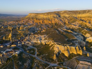 A picturesque landscape with rock formations and a small village in warm sunset light, aerial view,