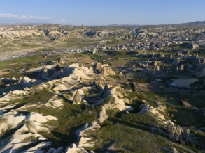 Vast landscape with striking rock formations and a village under a blue sky, aerial view, Göreme