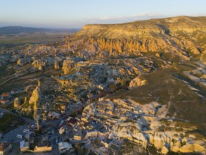 Stone formation at sunset over a village with a golden skyscape, aerial view, Göreme National Park,