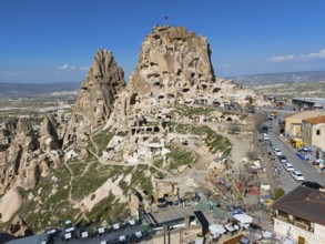 Historical rock formation with caves and buildings under a clear blue sky in a vast landscape,