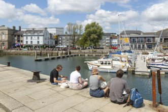 People sitting on quayside of marina harbour, The Barbican, Plymouth, Devon, England, UK