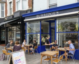 People sitting at tables on pavement outside Burridges cafe, Victoria Parade, Torquay, Devon,