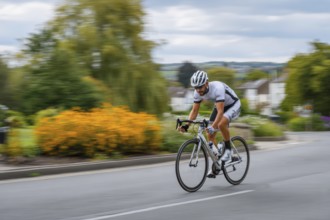 A cyclist, racing cyclist rides his racing bike fast on a road through a rural area, AI generated,