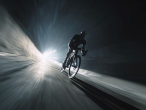 A cyclist, racing cyclist riding his racing bike fast on a sloping road in the dark, motion blur,