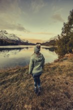 Woman by the lake in autumn Engadine in Switzerland with snow-covered mountain peaks