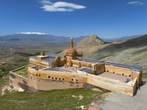 Majestic ancient fortress in front of a vast mountain panorama and deep blue sky, aerial view,