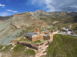 Old fortress embedded in dramatic mountain scene with cloudy sky and rocky heights, aerial view,