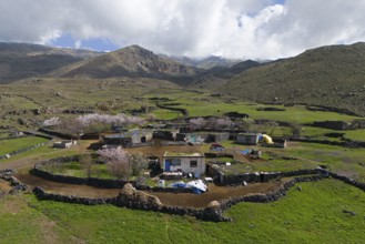Small village amidst green hills and blossoming trees under a cloudy sky, village at the foot of