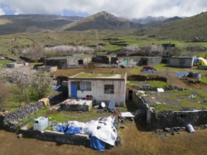 Rural village with simple houses and lots of greenery in mountainous terrain under a cloudy sky,