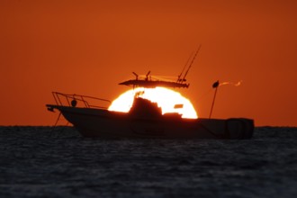 The sun rises behind a boat on the Costa Rei, a coastal stretch of the Italian Mediterranean island